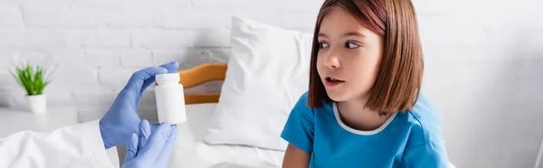 Pediatrician holding container with medicines near astonished girl in hospital, banner — Foto stock