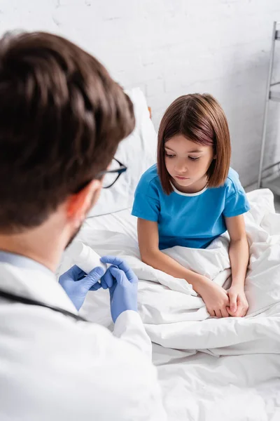 Doctor holding container with medicines near sick girl in hospital, blurred foreground — Stock Photo