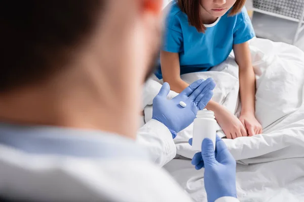 Обрізаний вид лікаря, що дає таблетку хворій дівчині в лікарні, розмитий передній план — стокове фото