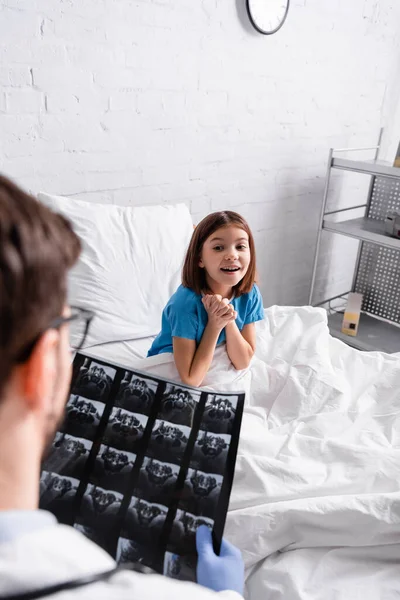Happy girl looking at doctor with x-ray on blurred foreground — Stock Photo