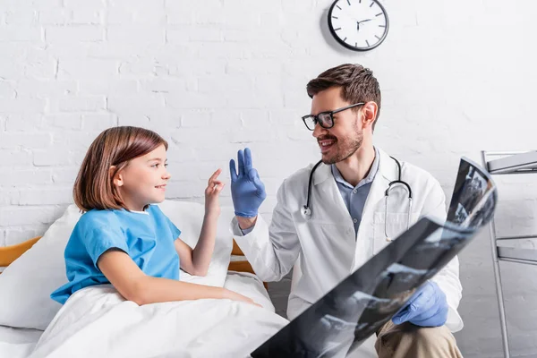 Menina feliz e médico mostrando sinal ok perto de raio-x no hospital — Fotografia de Stock