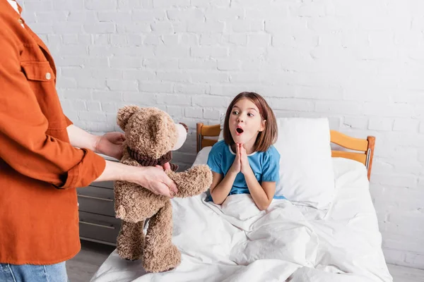 Excited girl showing wow gesture near dad holding teddy bear in hospital — Stock Photo