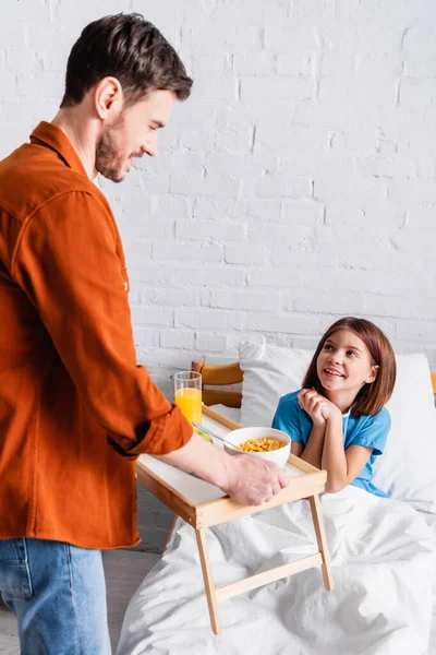 Homem sorrindo transportando bandeja com café da manhã perto da filha feliz — Fotografia de Stock