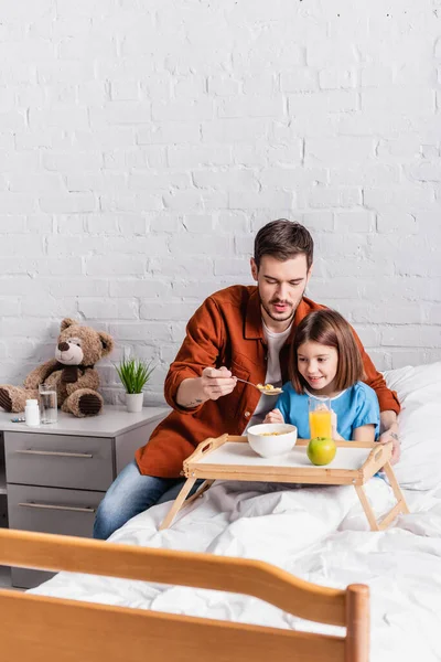 Father feeding daughter with cornflakes during breakfast in hospital — Stock Photo