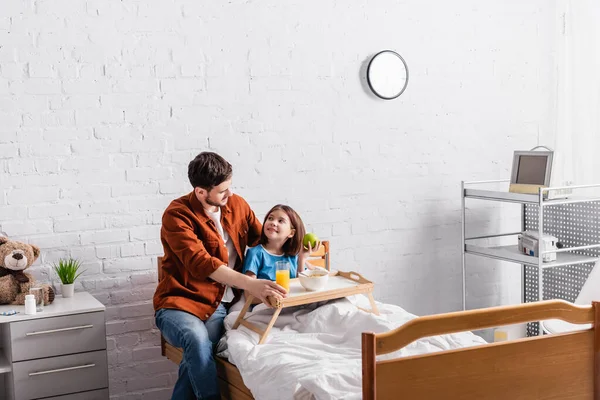 Happy father and daughter looking at other near tray with breakfast in hospital — Stock Photo