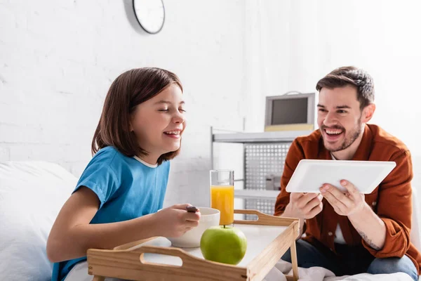 Excited girl laughing during breakfast in hospital near father with digital tablet — Stock Photo