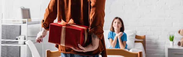 Back view of man holding gift box near joyful daughter in hospital bed on blurred background, banner — Stock Photo