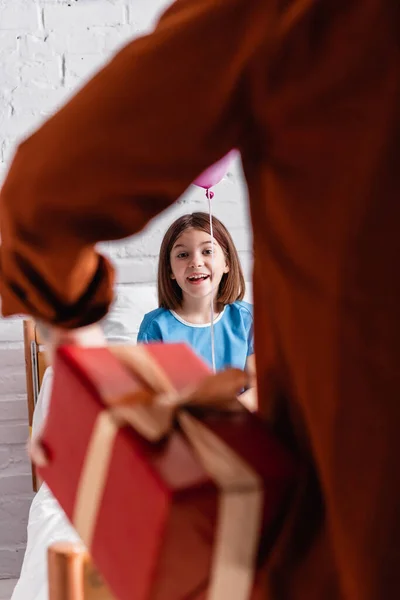 Erstauntes Mädchen blickt Vater mit Geschenkschachtel im verschwommenen Vordergrund an — Stockfoto