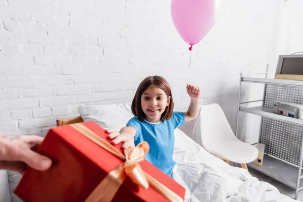 Cheerful girl holding festive balloon near father with gift box on blurred foreground — Stock Photo