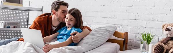 Père embrasser fille heureuse en utilisant un ordinateur portable dans le lit d'hôpital, bannière — Photo de stock
