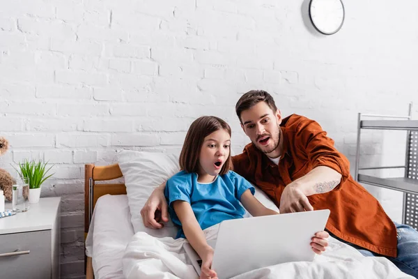 Verwunderter Mann zeigt auf Laptop neben verblüffter Tochter im Krankenhaus — Stockfoto