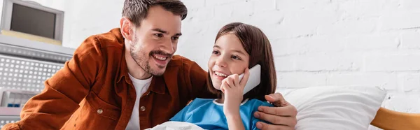 Glückliches Mädchen telefoniert im Krankenhaus in der Nähe von glücklichem Vater, Banner — Stockfoto