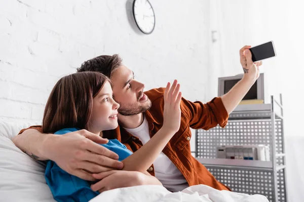 Fröhlicher Mann macht Selfie auf Smartphone mit Tochter im Krankenhaus — Stockfoto