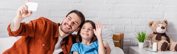 Glückliches Mädchen winkt Hand in Hand mit Papa macht Selfie auf Handy im Krankenhaus, Banner — Stockfoto