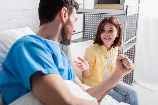 Smiling girl pointing at father showing win gesture in hospital bed — Stock Photo