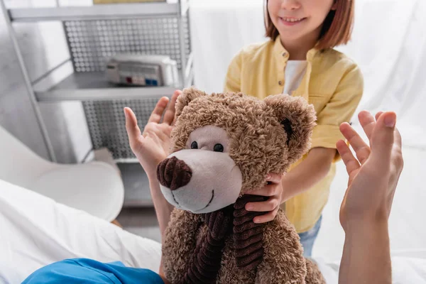 Обрезанный вид улыбающегося ребенка, держащего плюшевого мишку рядом с отцом в больнице — стоковое фото