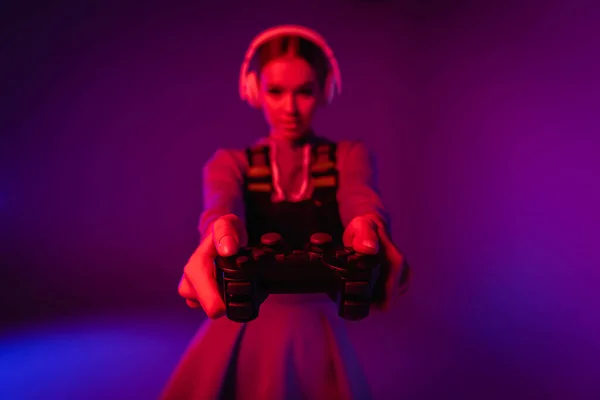 KYIV, UKRAINE - NOVEMBER 27, 2020: joystick in hands of young woman in headphones on blurred purple background — Stock Photo