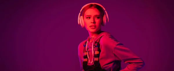 Jeune femme dans les écouteurs sans fil regardant loin sur fond violet, bannière — Photo de stock