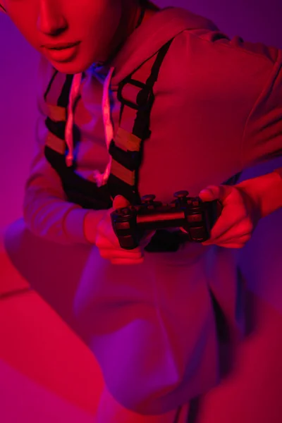 KYIV, UCRANIA - 27 de noviembre de 2020: vista recortada de una joven sosteniendo un joystick sobre púrpura - foto de stock