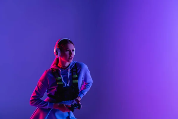 KYIV, UCRAINA - 27 NOVEMBRE 2020: donna in cuffia wireless con gamepad e videogiochi viola — Foto stock