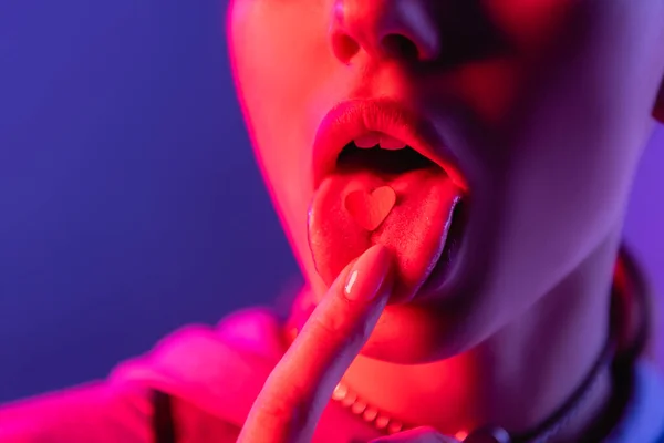 Vista cortada da mulher tocando a língua com o coração de papel isolado em roxo — Fotografia de Stock