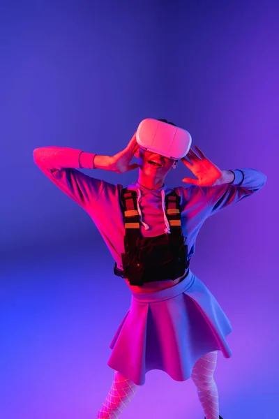Здивована молода жінка в гарнітурі віртуальної реальності на фіолетовому фоні — стокове фото