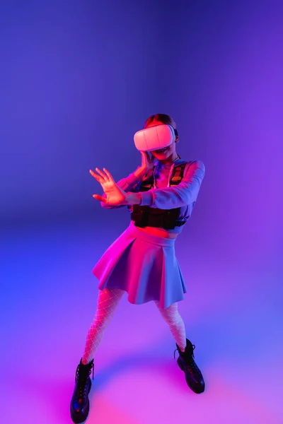 Full length of young woman in virtual reality headset gesturing on purple background — Stock Photo