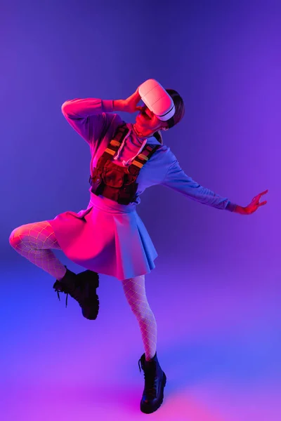 Full length of amazed woman in virtual reality headset gesturing and jumping on purple background — Stock Photo