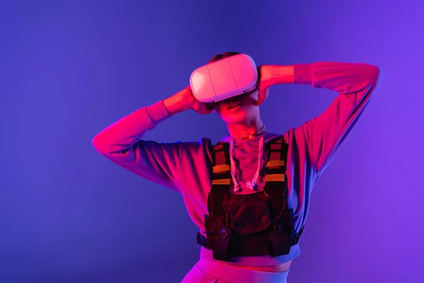 Young woman touching virtual reality headset on purple background — Stock Photo