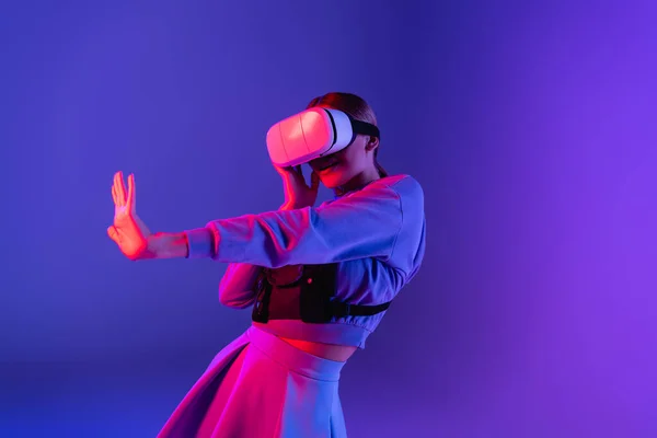 Woman in virtual reality headset gesturing on purple background — Stock Photo