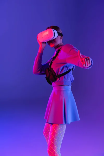 Jeune femme en réalité virtuelle casque pointant du doigt sur fond violet — Photo de stock