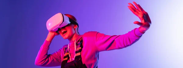 Excited young woman in virtual reality headset gesturing on purple background, banner — Stock Photo