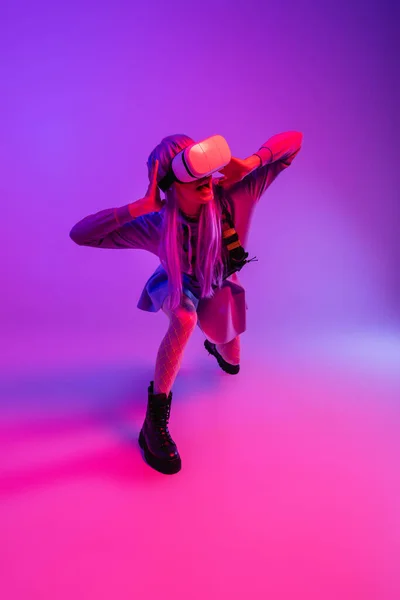 Volle Länge der verängstigten Frau in Virtual-Reality-Headset sitzt auf lila und rosa — Stockfoto
