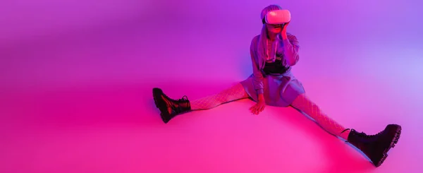 Comprimento total da mulher em fone de ouvido realidade virtual sentado em roxo com iluminação rosa, banner — Fotografia de Stock