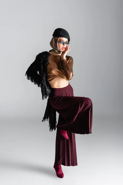 Pleine longueur de femme à la mode en lunettes de soleil et béret posant sur le gris — Photo de stock