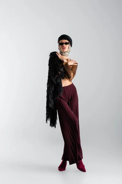 Full length of elegant woman in sunglasses and beret posing on grey — Stock Photo