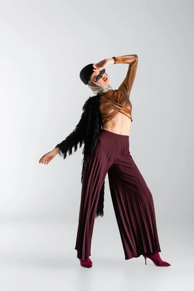 Full length of young woman in trendy sunglasses and beret posing on grey — Stock Photo