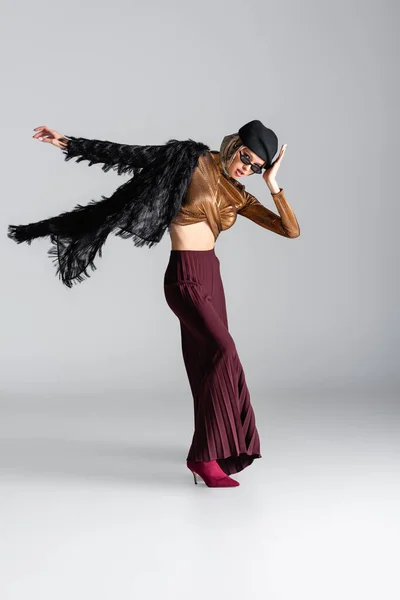 Pleine longueur de femme à la mode en lunettes de soleil et béret posant sur gris — Photo de stock