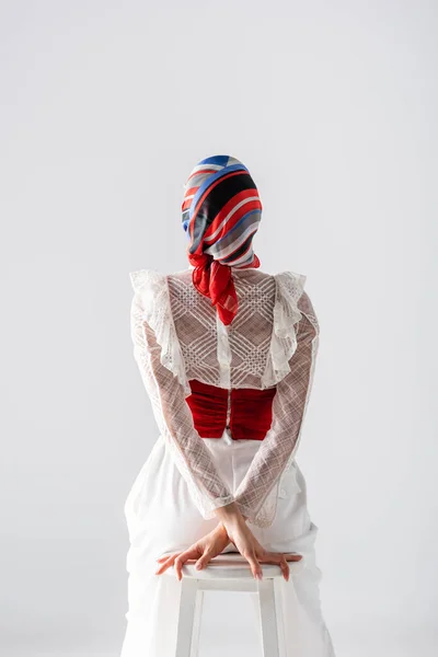 Back view of stylish woman in headscarf sitting on stool isolated on white — Stock Photo