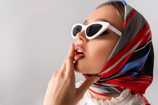 Молодая и чувственная женщина в платке и солнцезащитных очках касающихся губ, изолированных на белом — стоковое фото
