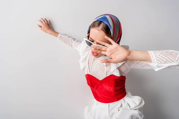 Vue grand angle de la jeune femme à la mode en foulard et lunettes de soleil gestuelle sur blanc — Photo de stock