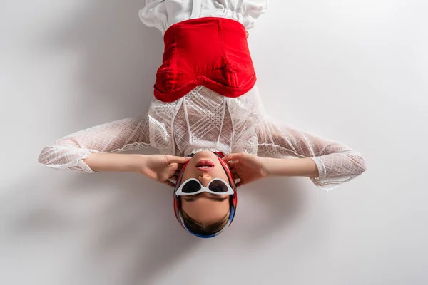 Top view of trendy woman in headscarf and sunglasses lying while looking at camera on white — стоковое фото