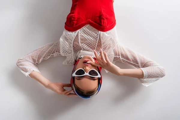 Top view of stylish woman in headscarf and sunglasses lying while looking at camera on white — Stock Photo