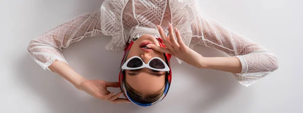Draufsicht auf trendige Frau mit Kopftuch und Sonnenbrille, die auf weißem Banner in die Kamera blickt — Stockfoto