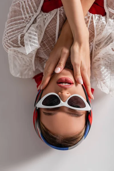 Top view of stylish woman in sunglasses and headscarf lying while looking at camera on white — стоковое фото