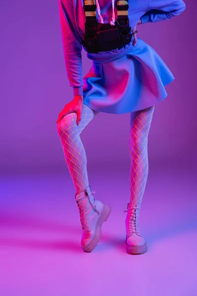 Обрезанный вид стильной женщины в юбке, стоящей с рукой на бедре на фиолетовый — стоковое фото