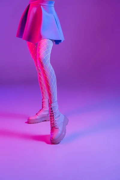 Vista cortada de mulher elegante em saia de pé em roxo com iluminação rosa — Fotografia de Stock