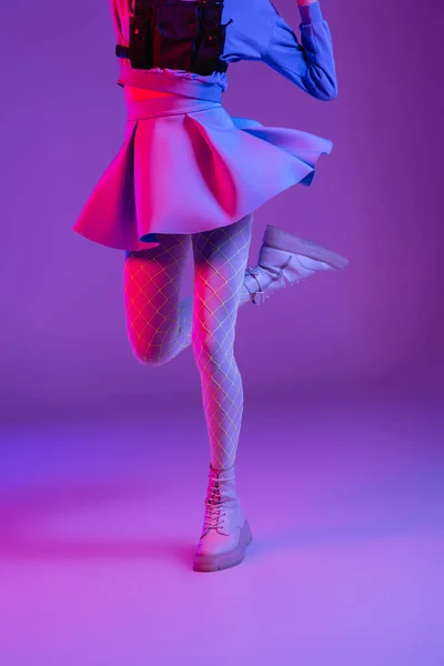 Обрезанный вид стильной женщины в юбке, прыгающей на фиолетовый с розовым освещением — стоковое фото