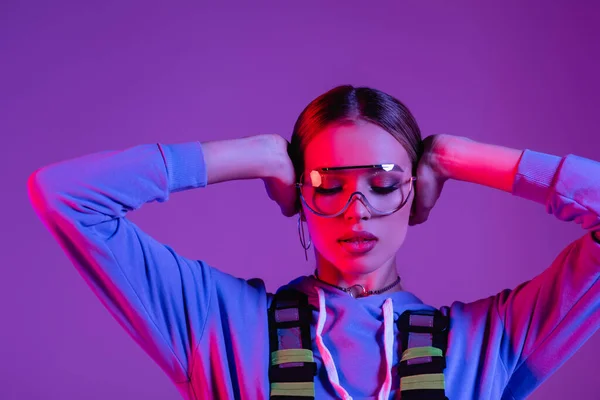 Молода стильна жінка в сонцезахисних окулярах і закритих очах ізольована на фіолетовому — стокове фото