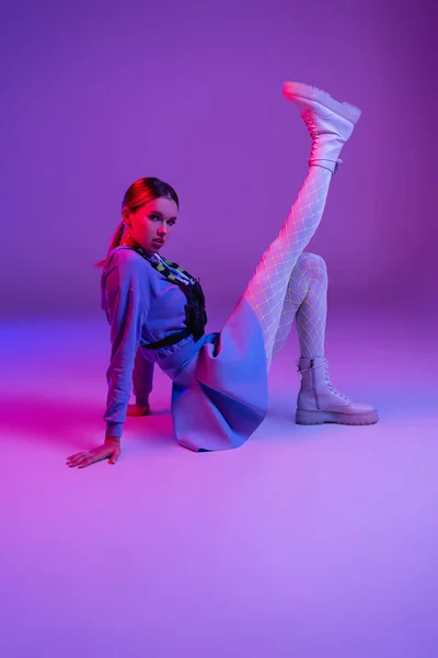 Повна довжина молодої стильної жінки в модному вбранні сидить на фіолетовому — стокове фото